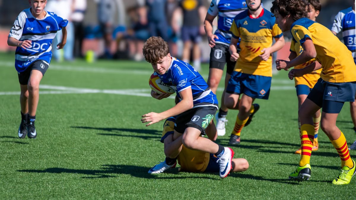 A dynamic capture of teenage rugby players in an intense match on a sunlit grass field.